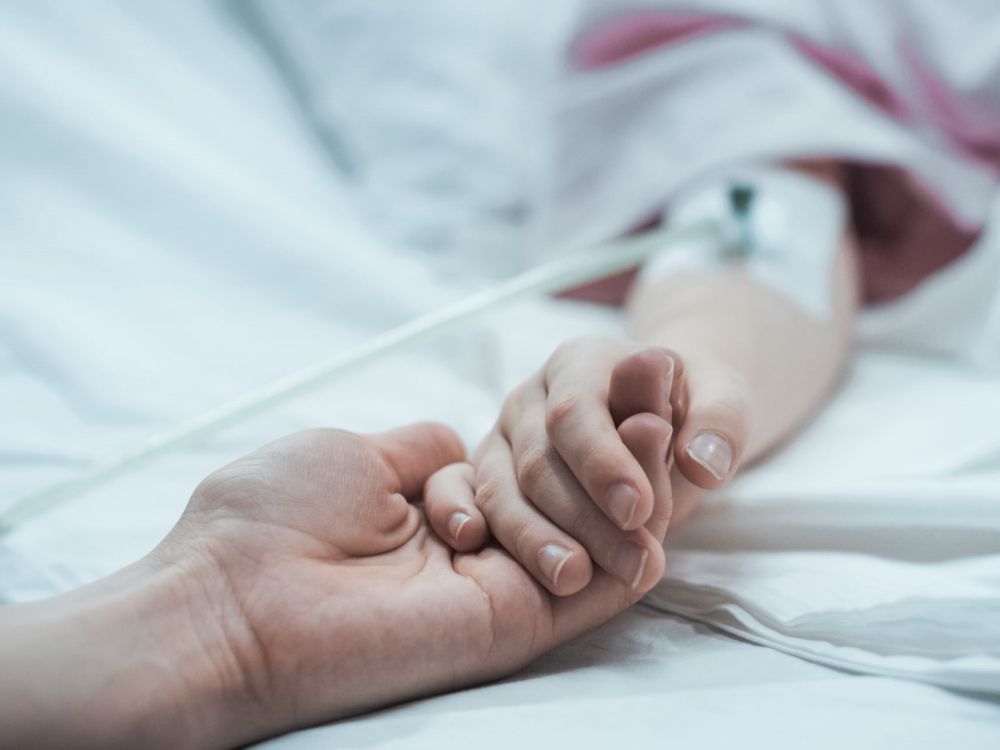 young child in hospital bed holds hands with support worker